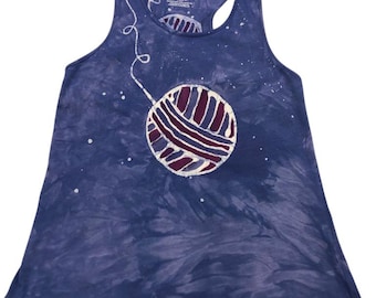 May include: A blue tie-dye tank top with a large yarn ball graphic. The yarn ball is white, burgundy, and purple. The tank top has a racerback design and the words "hand dyed" are visible.
