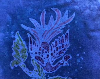 May include: A blue textile with a floral design. The central flower is light purple with red accents, surrounded by green leaves and stems. The background is a darker blue with lighter blue speckles.
