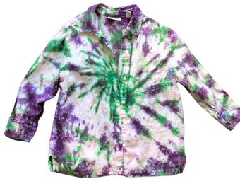 May include: A button-down shirt with a tie-dye pattern in white, green, and purple. The long-sleeved shirt has a collar and a pocket on the left side. The tie-dye design radiates from the center of the shirt.