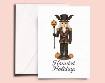 Könnte beinhalten: Halloween-Grußkarte mit einem Nussknacker in schwarzer und lila Uniform, Fledermausflügel-Hut und Kürbis-Zepter. Der Text "Haunted Holidays" und zwei kleine Kürbisse sind abgebildet.