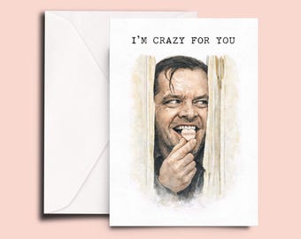 Op de afbeelding: Een wenskaart met de tekst "I'M CRAZY FOR YOU" boven een aquarel illustratie van een man die door een deur kijkt. De man houdt een hartvormig snoepje vast met het woord "obsessed". Links een witte envelop.