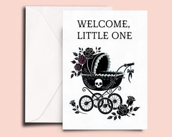 May include: A white greeting card and matching envelope featuring the text WELCOME, LITTLE ONE in black. The card displays a black baby carriage illustration adorned with a skull motif, dark roses, and a small bow, set against a plain white background.