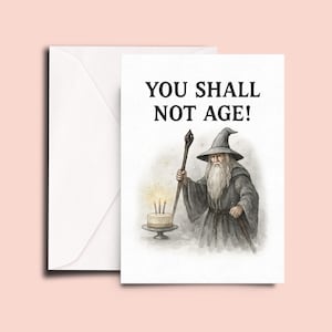 May include: A birthday card featuring a cartoon illustration of Gandalf from The Lord of the Rings, holding a staff and standing in front of a birthday cake with candles. The card reads "You shall not age!"