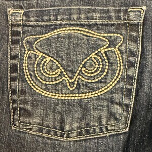 以下が含まれることがあります： 黒い持ち手と「But First, Coffee」のテキストが黒い太字で書かれた白いセラミックマグ。マグは白い表面に置かれています。マグの高さは約10cmです。