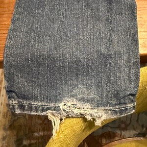 以下が含まれることがあります： 黒い持ち手と「But First, Coffee」の太字の黒い文字が入った白いセラミックマグカップ。マグカップはぼやけた背景に置かれ、居心地の良い環境を示唆しています。