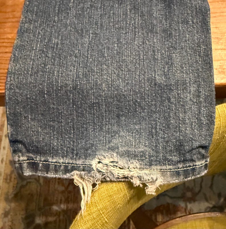 以下が含まれることがあります： 黒い持ち手と「But First, Coffee」の太字の黒い文字が入った白いセラミックマグカップ。マグカップはぼやけた背景に置かれ、居心地の良い環境を示唆しています。