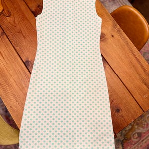 May include: A sleeveless dress featuring a white base with a repeating pattern of small, light green polka dots. The garment has a structured collar at the neckline and a straight, knee-length silhouette, showcasing a clean and simple design.