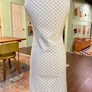 May include: A sleeveless knee-length dress featuring a white base with a repeating pattern of light teal polka dots. The garment includes a structured collar at the neckline and a straight-cut silhouette, displayed on a mannequin form.