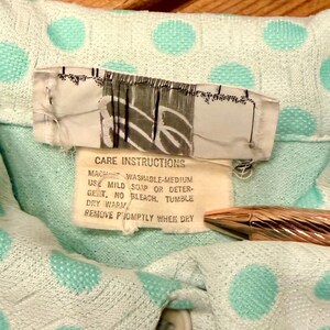 May include: A light mint green garment with a textured polka dot pattern. A white care label is attached, featuring the text: CARE INSTRUCTIONS, MACHINE WASHABLE-MEDIUM, USE MILD SOAP OR DETERGENT, NO BLEACH, TUMBLE DRY WARM, REMOVE PROMPTLY WHEN DRY.