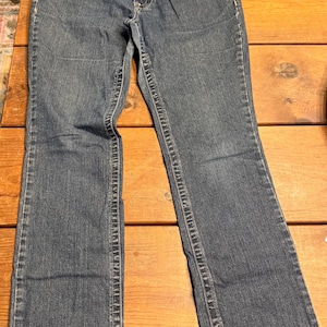 以下が含まれることがあります： クラシックな5ポケットデザインの青いデニムジーンズ。ジーンズはボタンとジッパーで開閉し、ベルトループがあり、少し色あせた外観です。脚はストレートで、裾にわずかなフレアがあります。