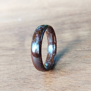 May include: A dark brown wooden ring with a light brown wood grain pattern. The ring has a smooth, polished finish.