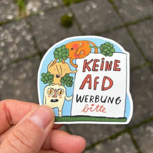 Könnte beinhalten: Ein Aufkleber mit Cartoon-Figuren und dem Text "KEINE AFD WERBUNG bitte". Die Figuren haben brokkoliartiges Haar. Der Text ist rot und schwarz auf weißem Hintergrund.