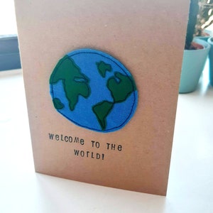¡Bienvenido al mundo! Motivo de globo bordado de movimiento libre montado en una tarjeta kraft marrón A6 reciclada