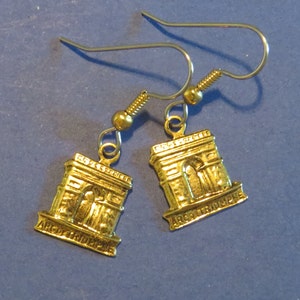 Op de afbeelding: Een paar gouden oorbellen met een miniatuurreplica van de Arc de Triomphe. Elke oorbel heeft een zilveren haak en een kleine gouden kraal aan de bovenkant.