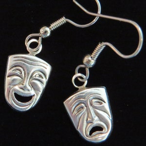 Op de afbeelding: Zilveren oorbellen met een ontwerp van een vrolijk en een verdrietig gezicht. De oorbellen zijn gemaakt van metaal en hebben een haaksluiting.