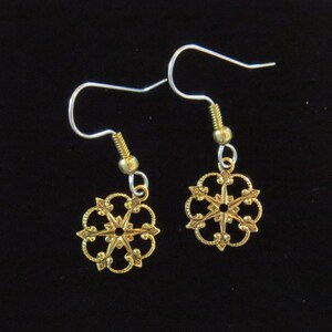 Può includere: Un paio di orecchini in filigrana color oro. Ogni orecchino presenta un delicato design traforato a forma di stella o fiocco di neve. Gli orecchini hanno ganci per le orecchie color argento e piccole perline color oro.