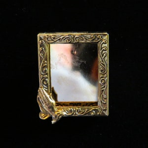 May include: A gold-colored picture frame with ornate detailing and a praying hands design. The frame is empty.