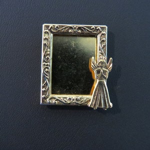 May include: A gold-toned metal picture frame with an ornate design. The frame has a blank space for a photo and features a small angel figurine with a crown on its head.