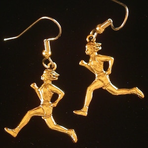 May include: A pair of gold-tone earrings featuring a runner figurine. The earrings are made of metal and have a hook closure.