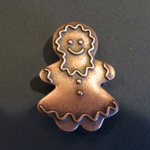 May include: A copper-coloured gingerbread person charm with a smiling face and a scalloped edge.