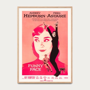 Puede incluir: Un póster enmarcado de la película "Funny Face" con Audrey Hepburn y Fred Astaire. El póster tiene una combinación de colores rosa y blanco con el título de la película en un lugar destacado. El póster está en un marco de madera.