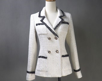 May include: A white tweed blazer with black trim and gold buttons. The blazer has a double-breasted closure and a v-neck.