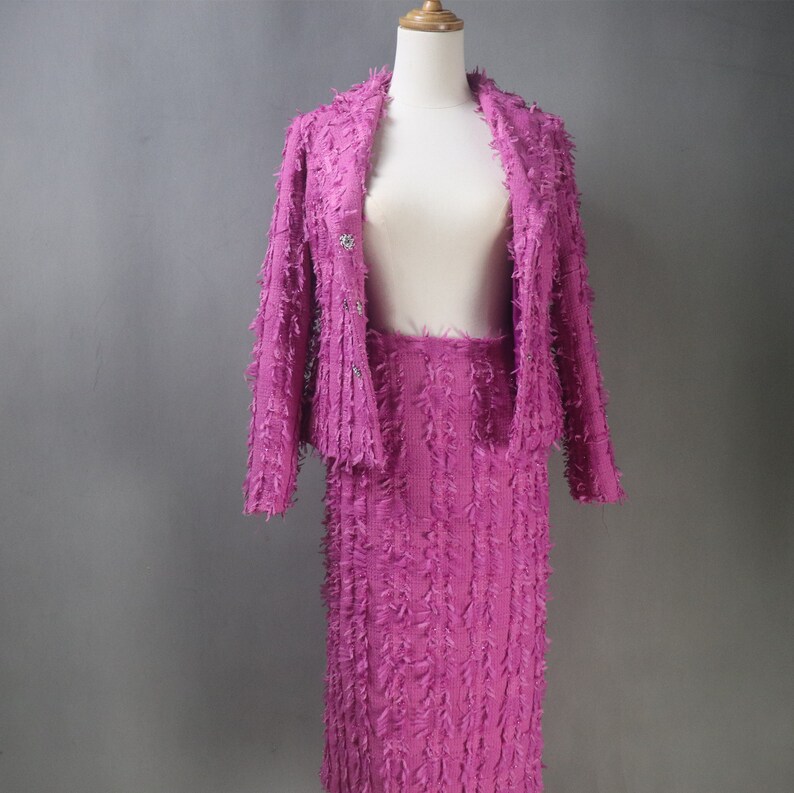 May include: A pink knit cardigan and skirt set with a textured, fuzzy finish. The cardigan has a button closure and the skirt is knee-length.