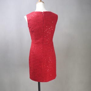 May include: A sleeveless red dress with a textured fabric and subtle sequin embellishments. The dress has a fitted silhouette and a zipper closure down the back. The dress is displayed on a mannequin.
