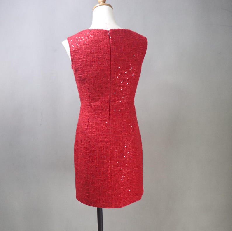 May include: A sleeveless red dress with a textured fabric and subtle sequin embellishments. The dress has a fitted silhouette and a zipper closure down the back. The dress is displayed on a mannequin.