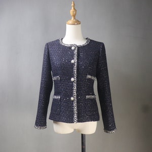 May include: A black tweed jacket with pearl-like buttons and a chain trim. The jacket has a fitted silhouette and long sleeves.