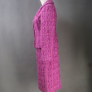 May include: A pink tweed skirt suit with a jacket and a skirt. The suit has a textured, frayed look.