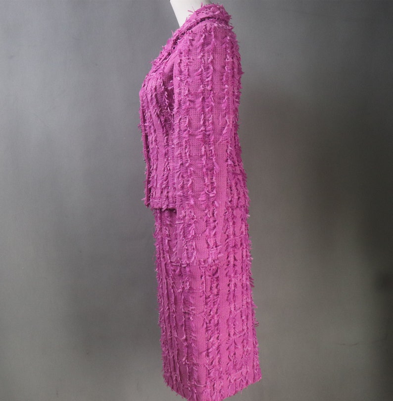 May include: A pink tweed skirt suit with a jacket and a skirt. The suit has a textured, frayed look.