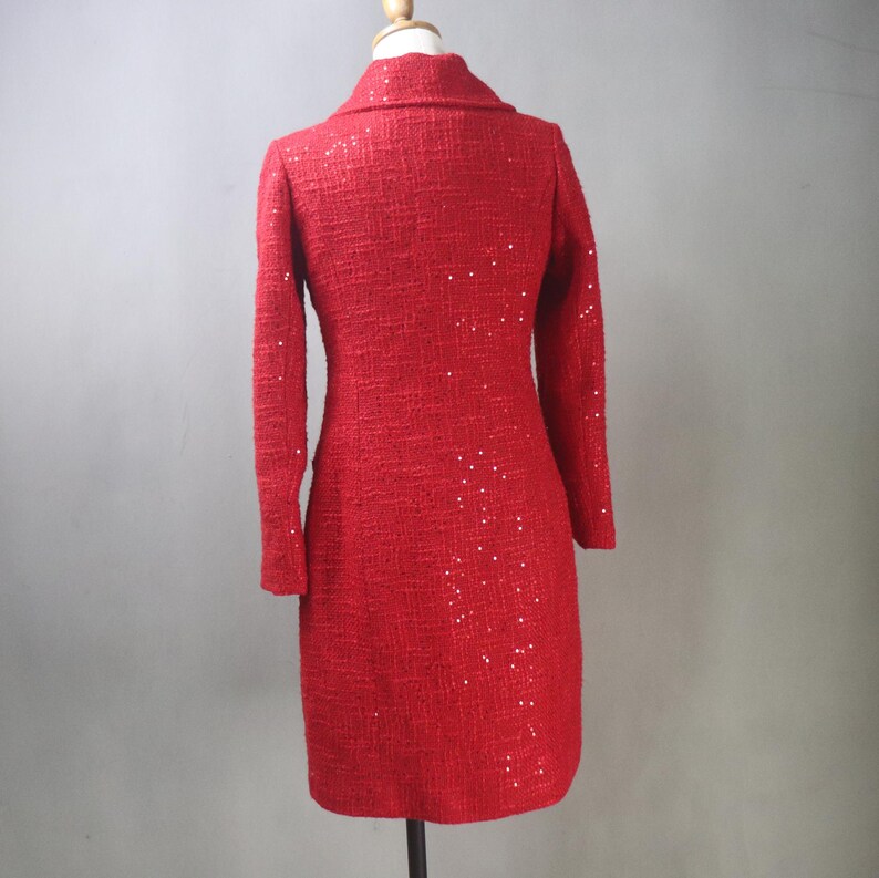 May include: A red tweed dress with long sleeves and a collared neckline. The dress is adorned with scattered sequins, adding a touch of sparkle. The dress is displayed on a mannequin.