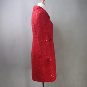 May include: A red tweed blazer with a classic collar and two front pockets. The blazer is adorned with scattered sequins, adding a touch of sparkle. The garment is displayed on a mannequin.