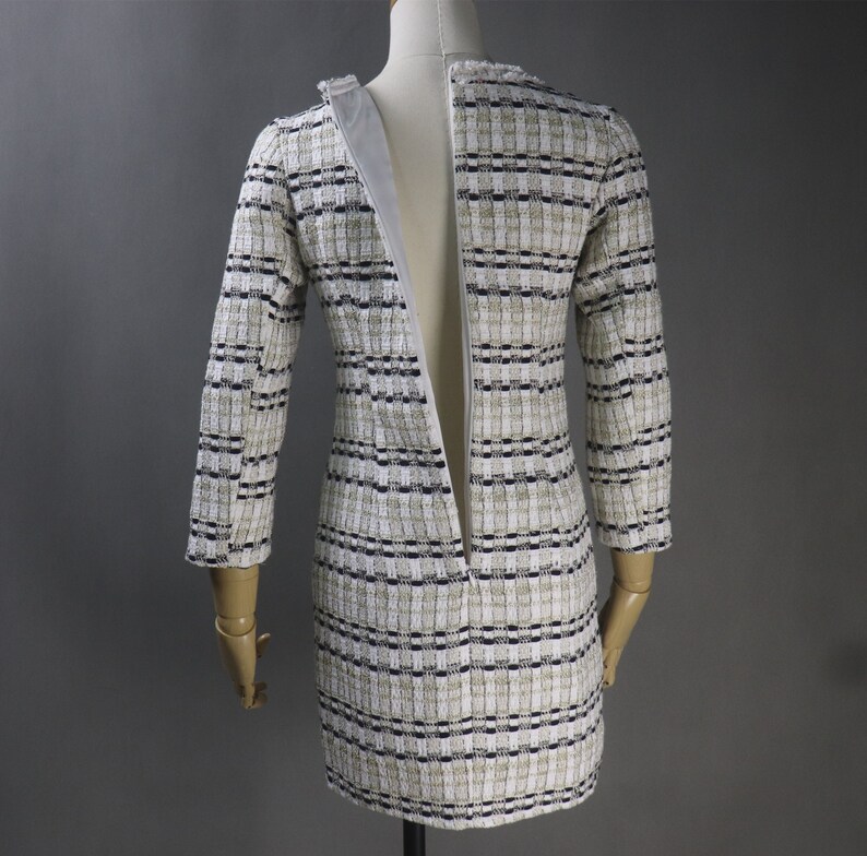 May include: A tweed dress with a cream, black, and tan checkered pattern. The dress has long sleeves and a zipper down the back. The dress is displayed on a mannequin.