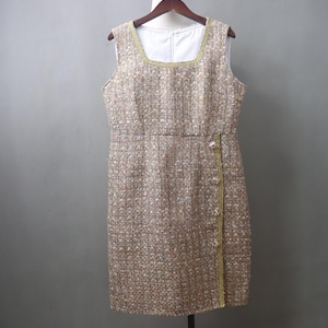 May include: Sleeveless tweed dress in a neutral color palette of beige, white, and gold. The dress features a square neckline, a fitted waist, and a straight skirt. Gold trim accents the neckline and the front closure. The dress is hanging on a wooden hanger.