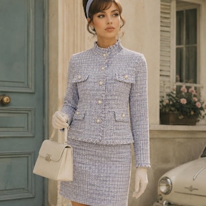 May include: A light blue tweed skirt suit with a matching jacket featuring pearl buttons and pockets. The outfit is paired with a cream-colored handbag and white gloves. The woman is wearing a light blue headband.
