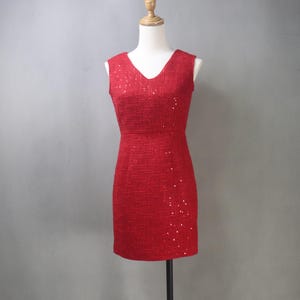 May include: A red, sleeveless dress with a V-neckline. The dress is made of a textured fabric and is adorned with scattered sequins. The dress is displayed on a mannequin.