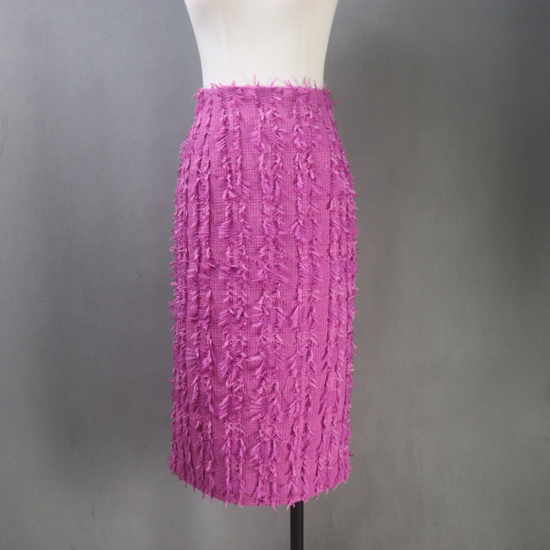 May include: A pink skirt with a fringe texture. The skirt is knee-length and has a straight silhouette.