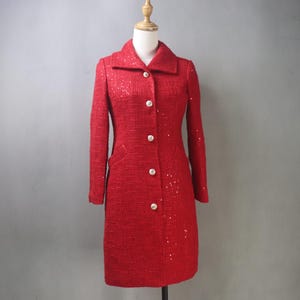 May include: A red, knee-length coat with a classic collar and long sleeves. The coat features large, gold-colored buttons and a textured fabric with subtle sequin accents. The coat is displayed on a mannequin.