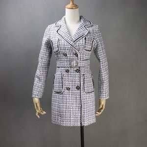 May include: A white and blue tweed dress with a black trim. The dress has a double-breasted closure, a belt, and two pockets.
