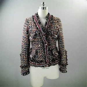 May include: A black, red, and blue tweed jacket with a fringed trim and pearl-like buttons. The jacket has a v-neck and a fitted silhouette.