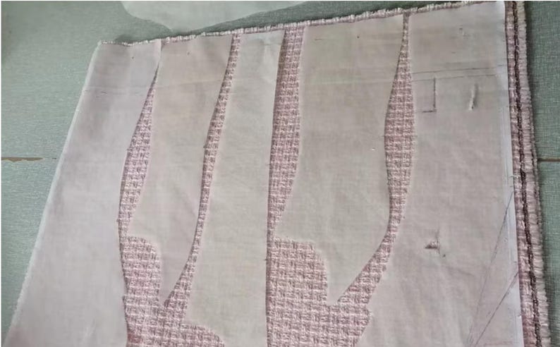 May include: A sewing project in progress, featuring fabric and pattern pieces. The fabric is a textured pink, and the pattern pieces are white, cut in curved shapes. The scene suggests garment construction.
