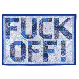 Könnte beinhalten: Eine blaue und weiße Patchwork-Decke mit den Worten "F**K OFF" in großen Buchstaben. Die Decke besteht aus verschiedenen Blumenmustern und ist von einem blauen Rand umgeben.