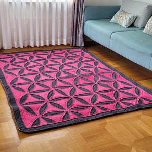 May include: A pink and grey patterned rug with a geometric design. The rug is on a wooden floor in a living room.