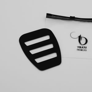May include: Black plastic strap with three slots, designed for holding items together. The strap is packaged in a clear plastic bag with the logo "TRANI DESIGNS" printed on it.