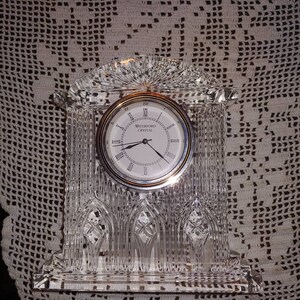 May include: A Waterford Crystal clock with a clear crystal base and a silver face with Roman numerals. The clock is in the shape of a church.