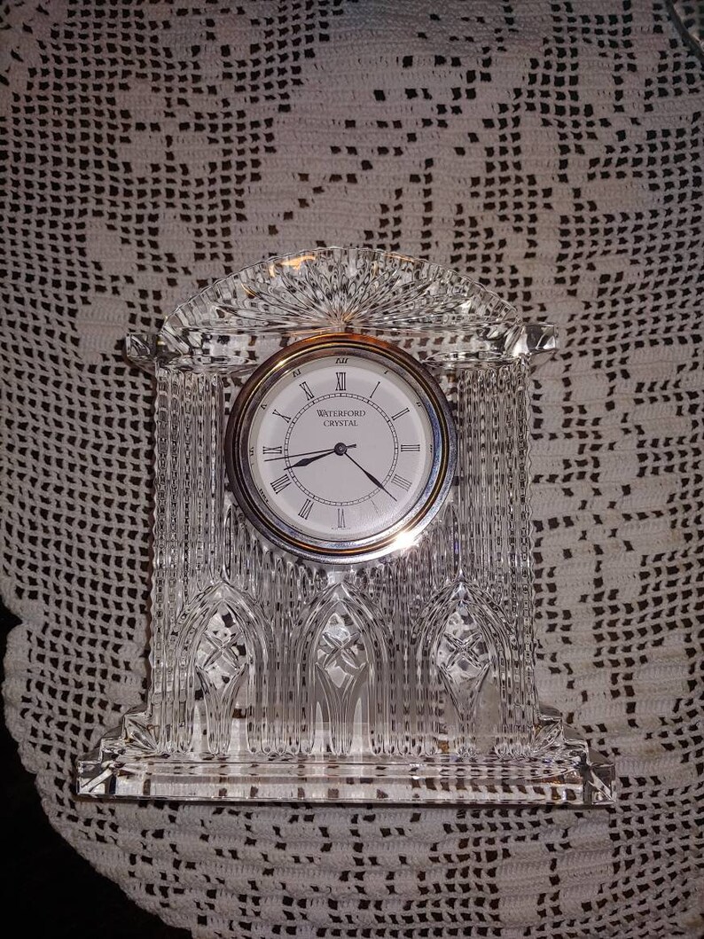 May include: A Waterford Crystal clock with a clear crystal base and a silver face with Roman numerals. The clock is in the shape of a church.