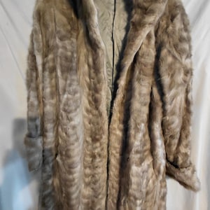 May include: A long, light brown fur coat with a large collar and long sleeves. The coat is open in the front, revealing a lighter-colored lining. The fur has a textured appearance, and the coat appears to be vintage.