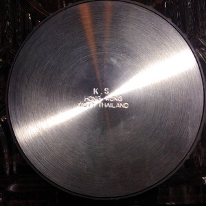 May include: A silver-colored metal disc with the text "K.S. HONG KONG MFG. THAILAND" engraved on the surface.